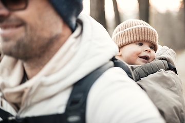 Image showing Sporty father carrying his infant son wearing winter jumpsuit and cap in backpack carrier hiking in autumn forest.