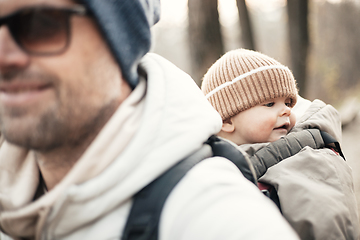 Image showing Sporty father carrying his infant son wearing winter jumpsuit and cap in backpack carrier hiking in autumn forest.