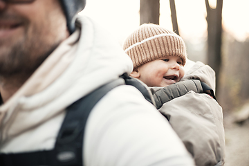 Image showing Sporty father carrying his infant son wearing winter jumpsuit and cap in backpack carrier hiking in autumn forest.