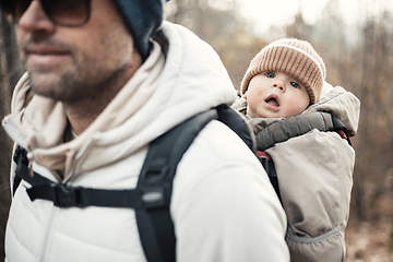 Image showing Sporty father carrying his infant son wearing winter jumpsuit and cap in backpack carrier hiking in autumn forest.