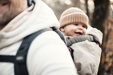 Image showing Sporty father carrying his infant son wearing winter jumpsuit and cap in backpack carrier hiking in autumn forest.