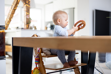 Image showing Happy infant sitting at dining table and playing with his toy in traditional scandinavian designer wooden high chair in modern bright atic home. Cute baby playing with toys