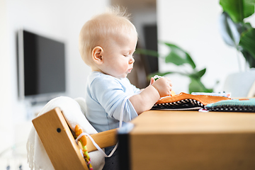 Image showing Happy infant sitting at dining table and playing with his toy in traditional scandinavian designer wooden high chair in modern bright atic home. Cute baby playing with toys