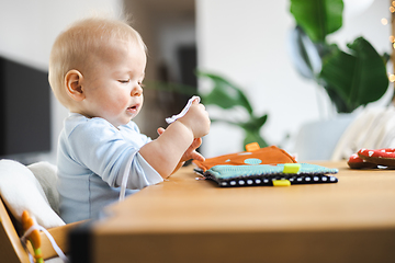 Image showing Happy infant sitting at dining table and playing with his toy in traditional scandinavian designer wooden high chair in modern bright atic home. Cute baby playing with toys