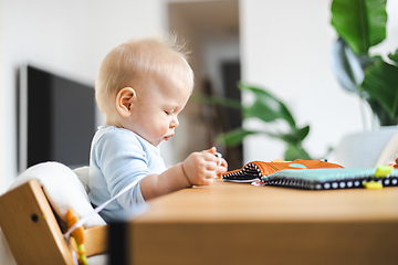 Image showing Happy infant sitting at dining table and playing with his toy in traditional scandinavian designer wooden high chair in modern bright atic home. Cute baby playing with toys