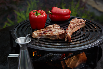 Image showing Tomahawk rib beef steak and T-bone on hot black grill.