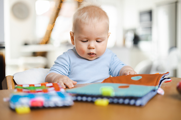 Image showing Happy infant sitting at dining table and playing with his toy in traditional scandinavian designer wooden high chair in modern bright atic home. Cute baby playing with toys