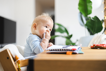 Image showing Happy infant sitting at dining table and playing with his toy in traditional scandinavian designer wooden high chair in modern bright atic home. Cute baby playing with toys