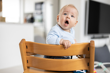 Image showing Happy infant sitting in traditional scandinavian designer wooden high chair in modern bright home. Cute baby.