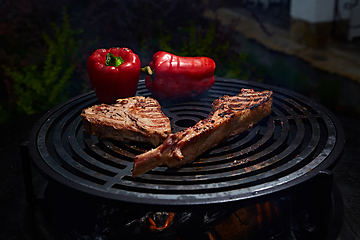 Image showing Tomahawk rib beef steak and T-bone on hot black grill.