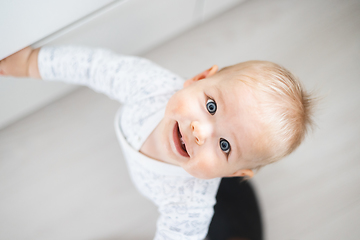 Image showing top down view of cheerful baby boy infant taking first steps holding to kitchen drawer at home. Cute baby boy learning to walk