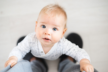 Image showing Top down view of cheerful baby boy infant taking first steps holding to father's sweatpants at home. Cute baby boy learning to walk