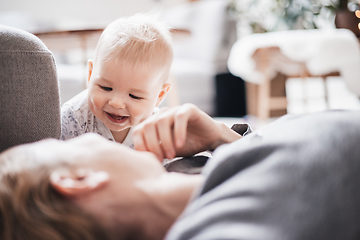 Image showing Happy family moments. Mother lying comfortably on children's mat playing with her baby boy watching and suppervising his first steps. Positive human emotions, feelings, joy.