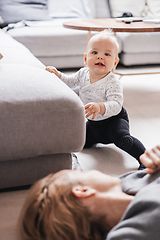 Image showing Happy family moments. Mother lying comfortably on children's mat playing with her baby boy watching and suppervising his first steps. Positive human emotions, feelings, joy.