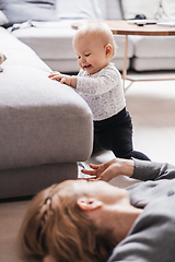 Image showing Happy family moments. Mother lying comfortably on children's mat playing with her baby boy watching and suppervising his first steps. Positive human emotions, feelings, joy.