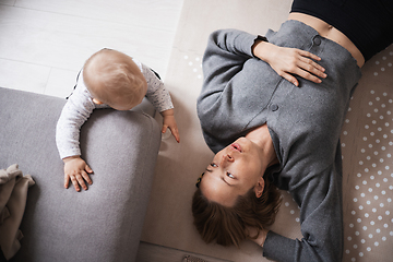 Image showing Happy family moments. Mother lying comfortably on children's mat playing with her baby boy watching and suppervising his first steps. Positive human emotions, feelings, joy.