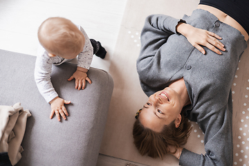 Image showing Happy family moments. Mother lying comfortably on children's mat playing with her baby boy watching and suppervising his first steps. Positive human emotions, feelings, joy.