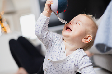 Image showing Cute infant baby boy playing, crawling and standing up by living room sofa at home. Baby playing at home