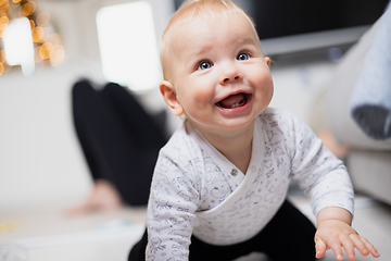 Image showing Cute infant baby boy playing, crawling and standing up by living room sofa at home. Baby playing at home.