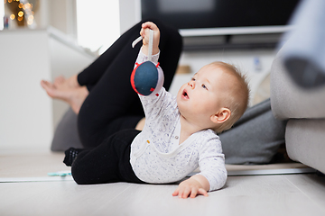 Image showing Happy family moments. Mother lying comfortably on children's mat watching and suppervising her baby boy playinghis in living room. Positive human emotions, feelings, joy