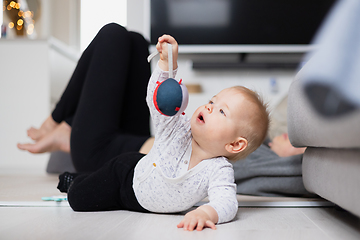 Image showing Happy family moments. Mother lying comfortably on children's mat watching and suppervising her baby boy playinghis in living room. Positive human emotions, feelings, joy