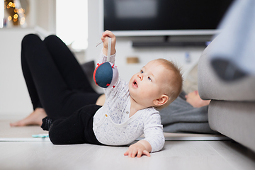 Image showing Happy family moments. Mother lying comfortably on children's mat watching and suppervising her baby boy playinghis in living room. Positive human emotions, feelings, joy