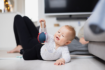 Image showing Happy family moments. Mother lying comfortably on children's mat watching and suppervising her baby boy playinghis in living room. Positive human emotions, feelings, joy