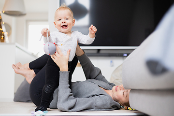 Image showing Happy family moments. Mother lying comfortably on children's mat playing with her baby boy watching and suppervising his first steps. Positive human emotions, feelings, joy.