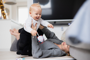 Image showing Happy family moments. Mother lying comfortably on children's mat playing with her baby boy watching and suppervising his first steps. Positive human emotions, feelings, joy.