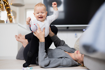 Image showing Happy family moments. Mother lying comfortably on children's mat playing with her baby boy watching and suppervising his first steps. Positive human emotions, feelings, joy.