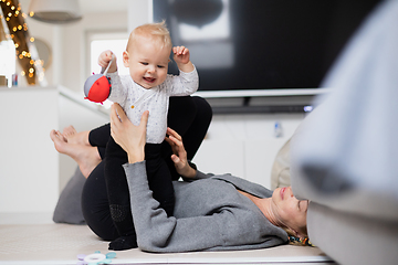 Image showing Happy family moments. Mother lying comfortably on children's mat playing with her baby boy watching and suppervising his first steps. Positive human emotions, feelings, joy.