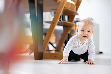 Image showing Cute infant baby boy crawling under dining room table at home. Baby playing at home