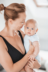 Image showing Portrait of sweet baby resting in mothers arms, looking at camera. New mom holding and cuddling little kid, embracing child with tenderness, love, care. Motherhood concept