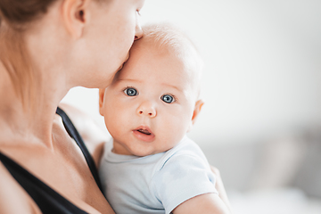 Image showing Portrait of sweet baby resting in mothers arms, looking at camera. New mom holding and kissing little kid, embracing child with tenderness, love, care. Motherhood concept