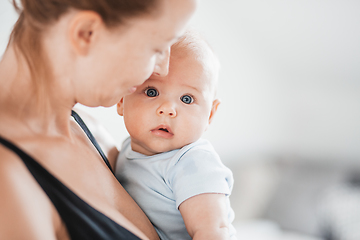 Image showing Portrait of sweet baby resting in mothers arms, looking at camera. New mom holding and cuddling little kid, embracing child with tenderness, love, care. Motherhood concept