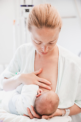 Image showing New mother carefully breastfeeds her newborn baby boy in hospital a day after labour.