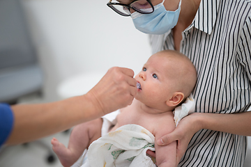 Image showing Pediatrician administring oral vaccination against rotavirus infection to little baby in presence of his mother. Children health care and disease prevention