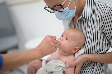 Image showing Pediatrician administring oral vaccination against rotavirus infection to little baby in presence of his mother. Children health care and disease prevention