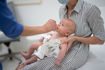 Image showing Pediatrician administring oral vaccination against rotavirus infection to little baby in presence of his mother. Children health care and disease prevention