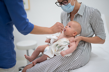 Image showing Pediatrician administring oral vaccination against rotavirus infection to little baby in presence of his mother. Children health care and disease prevention