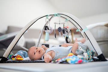 Image showing Cute baby boy playing with hanging toys arch on mat at home Baby activity and play center for early infant development. Baby playing at home