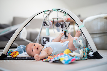 Image showing Cute baby boy playing with hanging toys arch on mat at home Baby activity and play center for early infant development. Baby playing at home