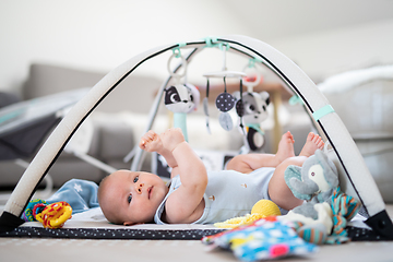 Image showing Cute baby boy playing with hanging toys arch on mat at home Baby activity and play center for early infant development. Baby playing at home