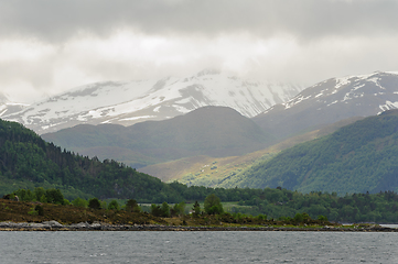 Image showing snow-capped mountains with green trees and rays of sunshine brea