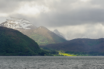 Image showing snow-covered mountains with green trees and rays of sunlight bre