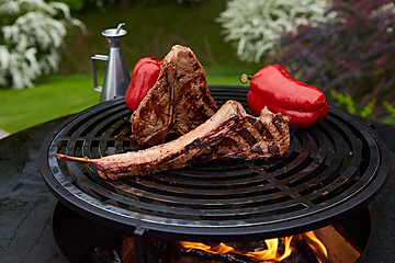 Image showing Tomahawk rib beef steak and T-bone on hot black grill.