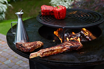 Image showing Tomahawk rib beef steak and T-bone on hot black grill.