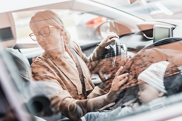 Image showing Mother reversing family car, looking for free parking space while running errands with her baby sleeping in infant car seat by her site.