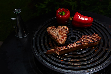 Image showing Tomahawk rib beef steak and T-bone on hot black grill.