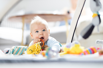 Image showing Cute baby boy playing with hanging toys arch on mat at home Baby activity and play center for early infant development. Baby playing at home